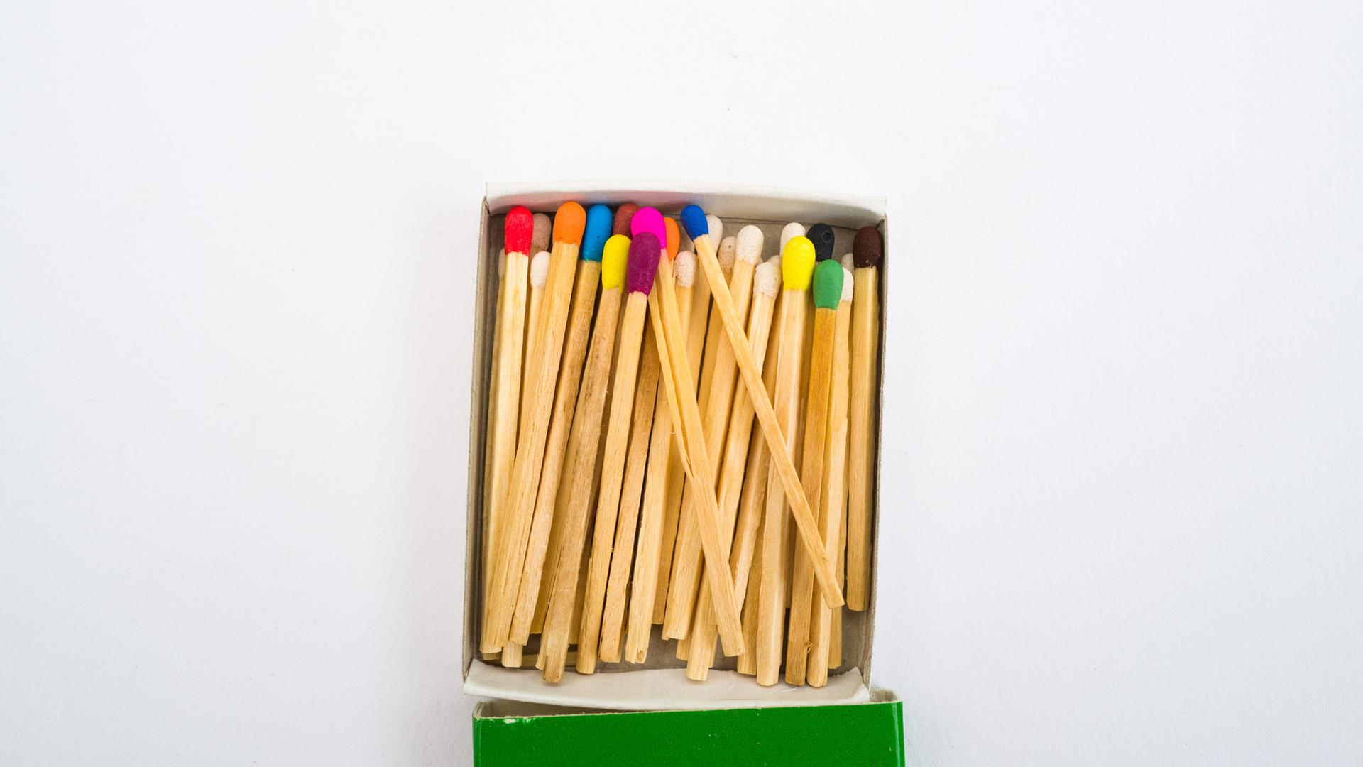 Streichhölzer mit verschiedenfarbigen Köpfen in einer geöffneten Schachtel vor hellem Hintergrund