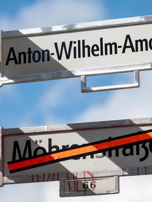 Ein Schild mit der Aufschrift Anton-Wilhelm-Amo-Straße hängt über einem Schild, auf dem der Name Mohrenstraße durchgestrichen ist