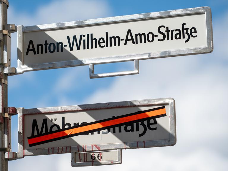 Ein Schild mit der Aufschrift Anton-Wilhelm-Amo-Straße hängt über einem Schild, auf dem der Name Mohrenstraße durchgestrichen ist