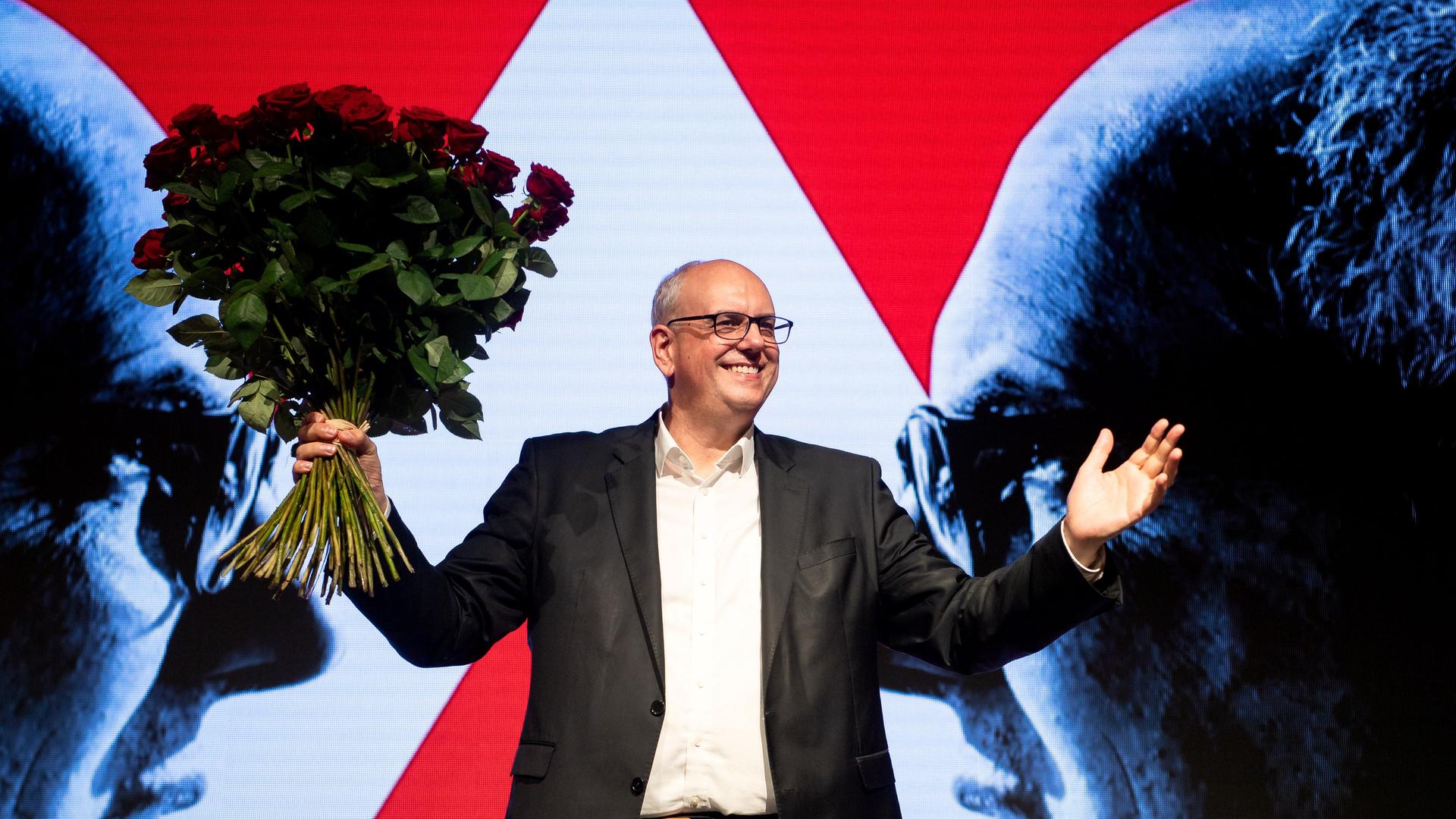 Der Bremer Bürgermeister Bovenschulte steht auf einer Bühne und hält einen großen Strauß roter Rosen in die Luft. Der Bremer Bürgermeister Bovenschulte steht auf einer Bühne und hält einen großen Strauß roter Rosen in die Luft.