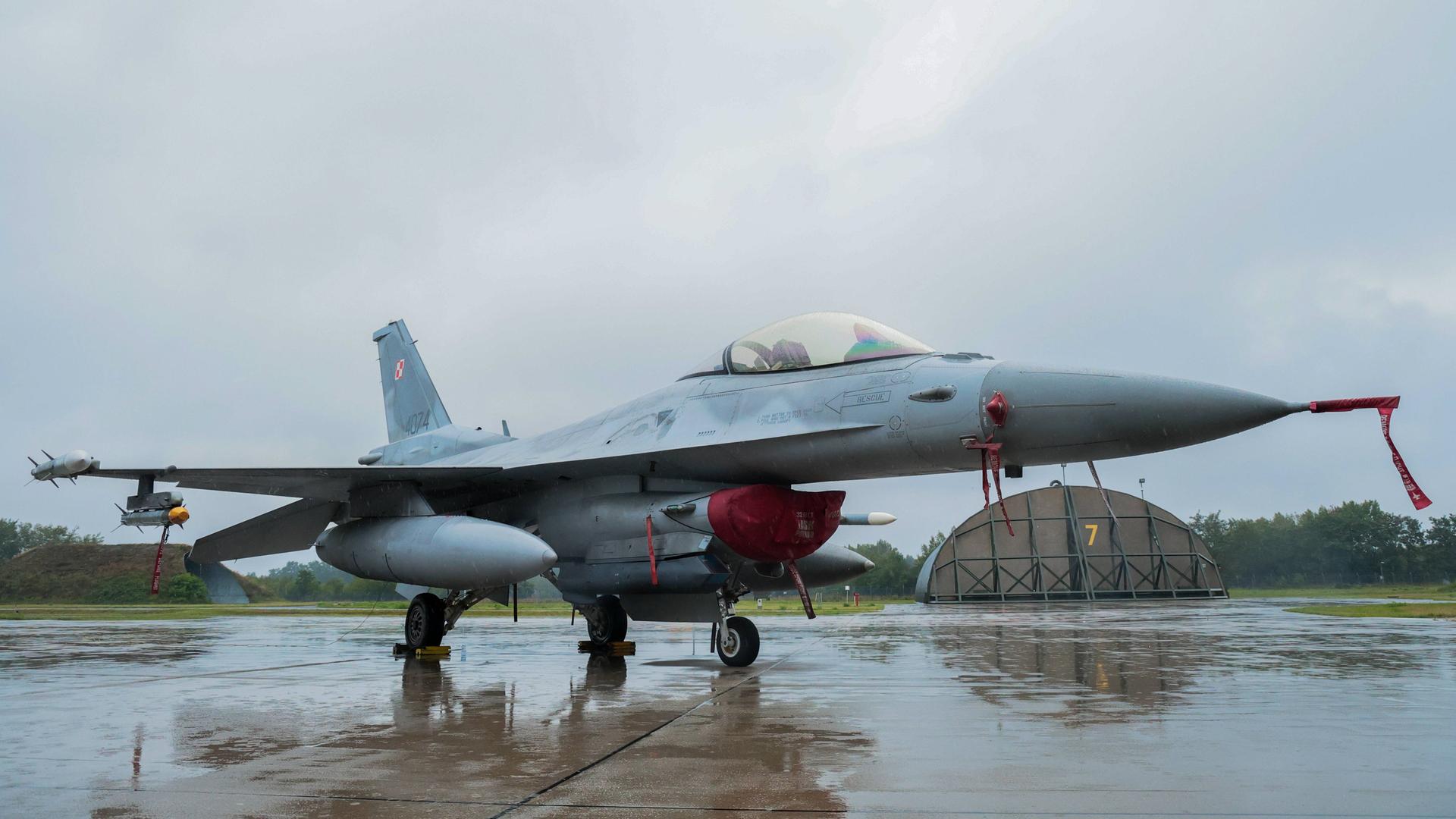 Ein Kampfjet steht auf einem Rollfeld auf der polnischen Militärbasis in Lask. Der Boden ist nass vom Regen, im Hintergrund graue Wolken. Ein Kampfjet steht auf einem Rollfeld auf der polnischen Militärbasis in Lask. Der Boden ist nass vom Regen, im Hintergrund graue Wolken.