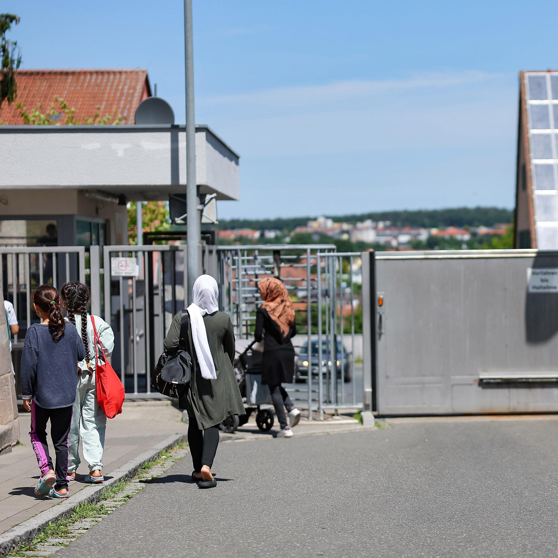 Einige Menschen gehen in der Zentralen Aufnahmeeinrichtung für Asylbewerber in Bayern auf ein geschlossenes, vergittertes Tor zu.