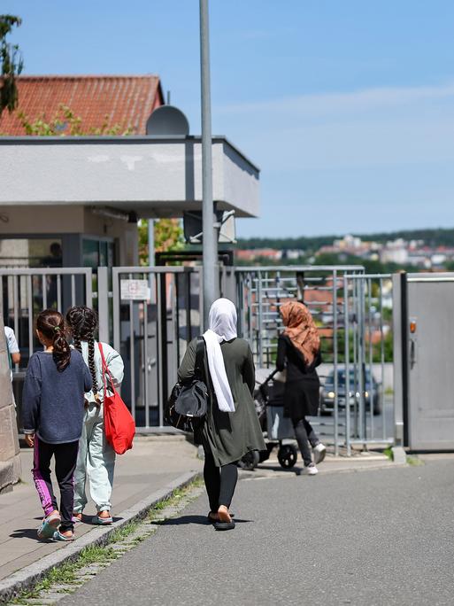 Einige Menschen gehen in der Zentralen Aufnahmeeinrichtung für Asylbewerber in Bayern auf ein geschlossenes, vergittertes Tor zu.