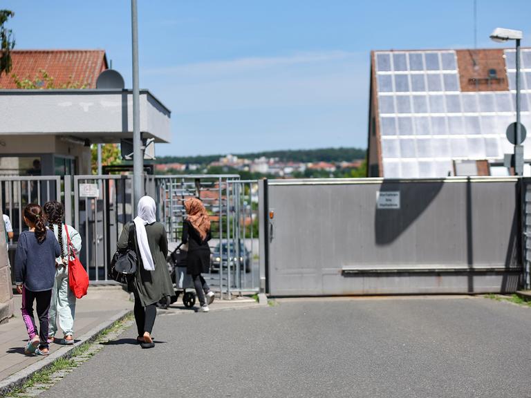 Einige Menschen gehen in der Zentralen Aufnahmeeinrichtung für Asylbewerber in Bayern auf ein geschlossenes, vergittertes Tor zu.