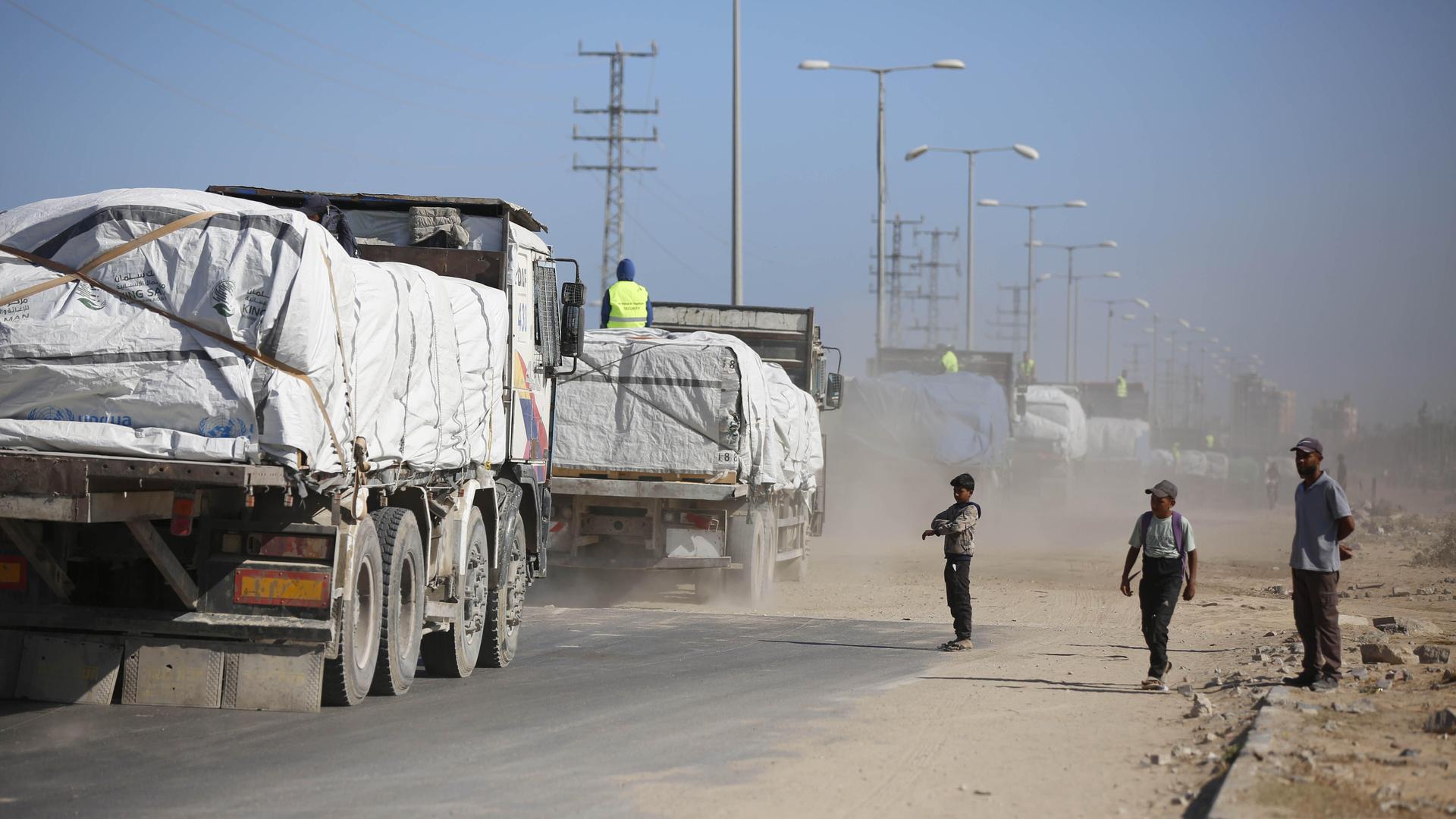 Ein Konvoi von Lkws mit Hilfsgütern fahren am 14.10.2025 in den Gazastreifen. Am Straßenrand stehen zwei Kinder und ein Mann. Ein Konvoi von Lkws mit Hilfsgütern fahren am 14.10.2025 in den Gazastreifen. Am Straßenrand stehen zwei Kinder und ein Mann.
