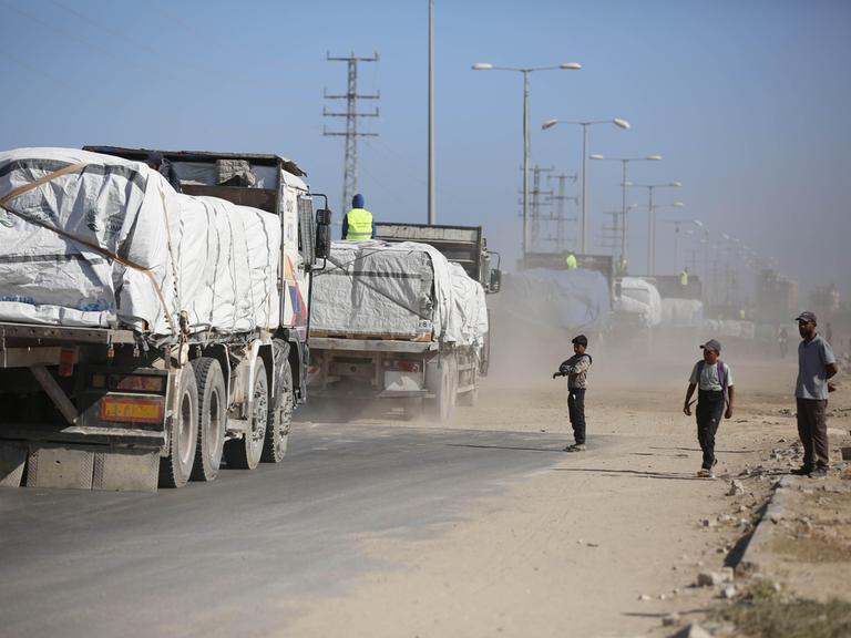 Ein Konvoi von Lkws mit Hilfsgütern fahren am 14.10.2025 in den Gazastreifen. Am Straßenrand stehen zwei Kinder und ein Mann.