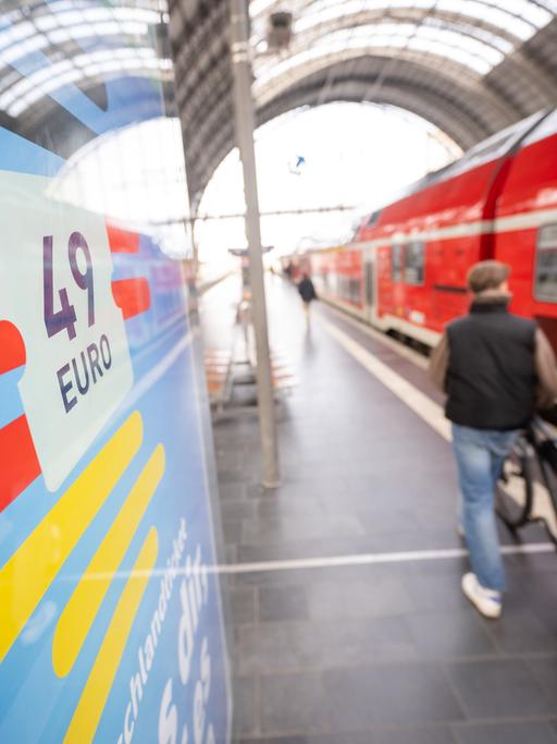 Ein Mann geht am Hauptbahnhof mit seinem Fahrrad zwischen der Werbung für das Deutschlandticket und einer Regionalbahn vorbei.