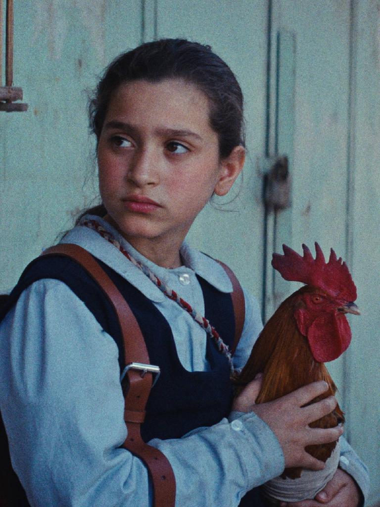 Ein Mädchen sitzt auf einer Bank und hält auf ihrem Schoß einen Hahn (Szenenbild aus dem Film "Ein Kuchen für den Präsidenten")