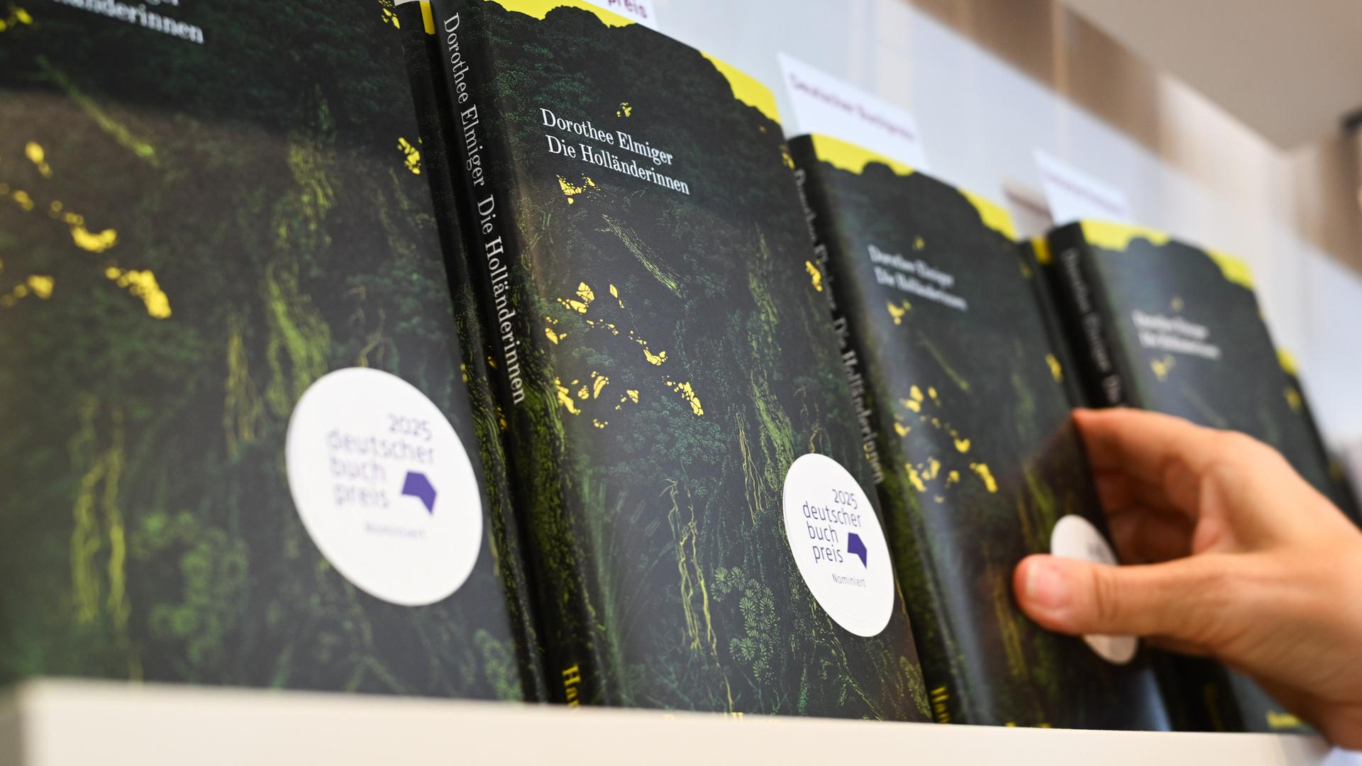 Eine Hand greift am Stand des Hanser Verlags auf der Frankfurter Buchmesse nach dem Buch der Schweizer Autorin Dorothee Elmiger mit dem Titel "Die Holländerinnen", dem Siegertitel beim Deutschen Buchpreis 2025.