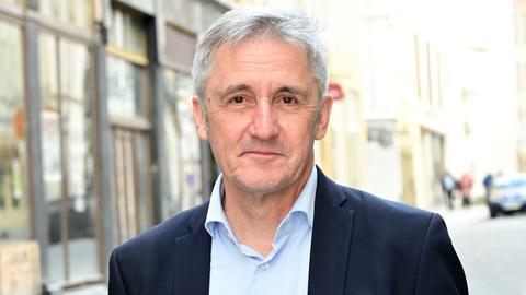 Ein Mann, Frank Richter, steht auf einer gepflasterten Straße, im Hintergrund sind Häuserfasaden zu sehen