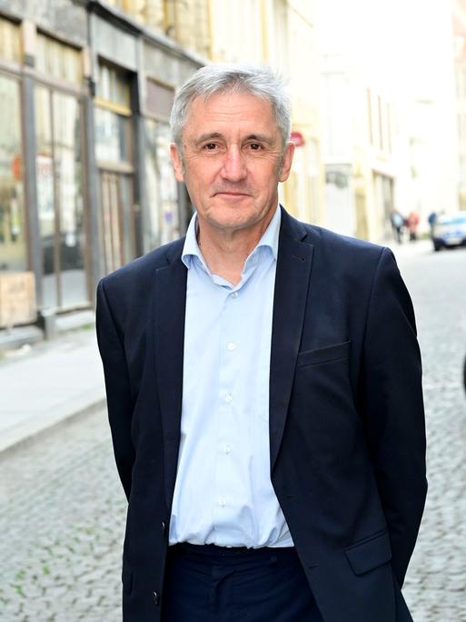 Ein Mann, Frank Richter, steht auf einer gepflasterten Straße, im Hintergrund sind Häuserfasaden zu sehen