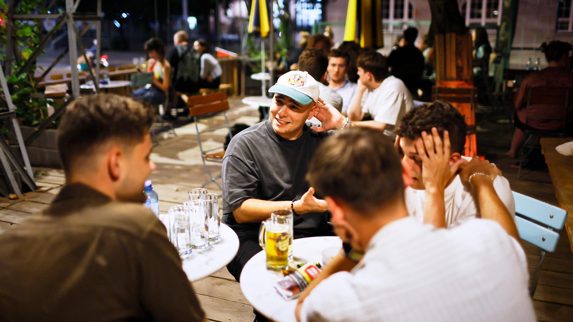 Junge Menschen sitzen im Außenbereich einer Kneipe bei Getränken.