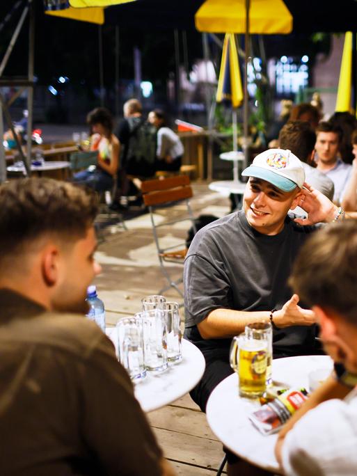 Junge Menschen sitzen im Außenbereich einer Kneipe bei Getränken.