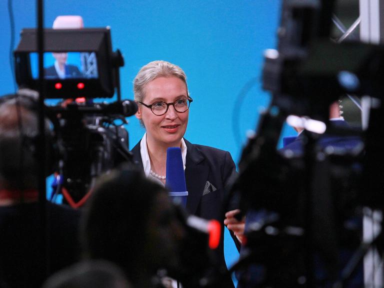 Die AfD-Co-Vorsitzende Alice Weidel steht vor zwei Kameras und spricht in ein Mikrofon während eines Interviews.