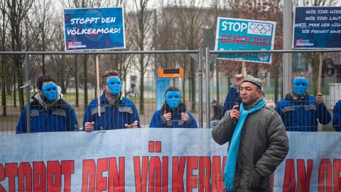 Asgar Can, Vorsitzender der Ostturkistanischen Union Uigurische Gemeinde bei einer Rede waehrend einer Kundgebung vor dem Bundeskanzleramt im Bezirk Berlin-Mitte. Dahinter protestieren maskierte Demonstranten der Aktivistengruppe Die Jungen Gerechten mit Transparenten und Protestplakaten gegen den Voelkermord an den Uiguren in der chinesischen autonomen Region Xinjiang und der Einhaltung der Menschenrechte und fordern einen diplomatischen Boykott der Olympischen Winterspiele 2022 in Peking.