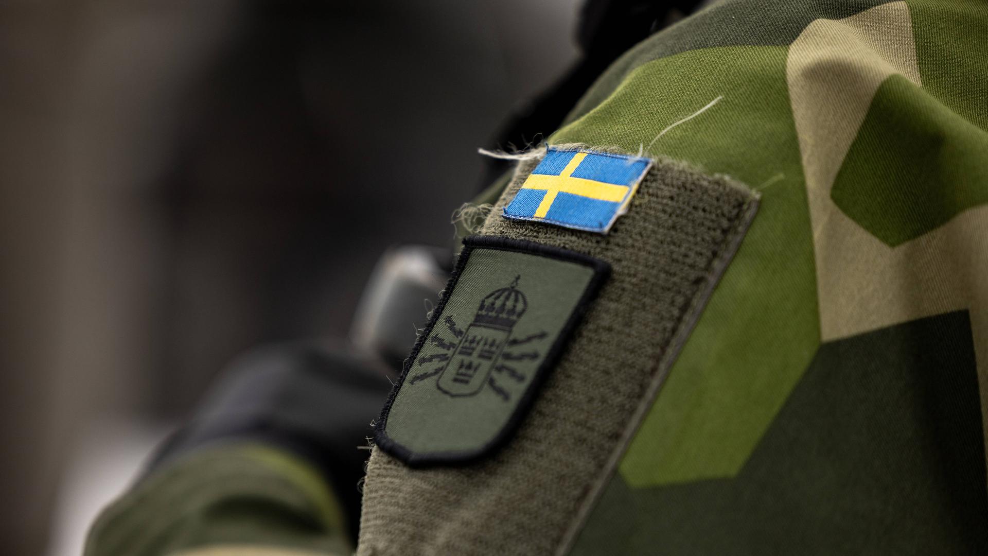 Zu sehen ist ein Soldat mit einer Uniform. Darauf zu sehen ist die schwedische Flagge.