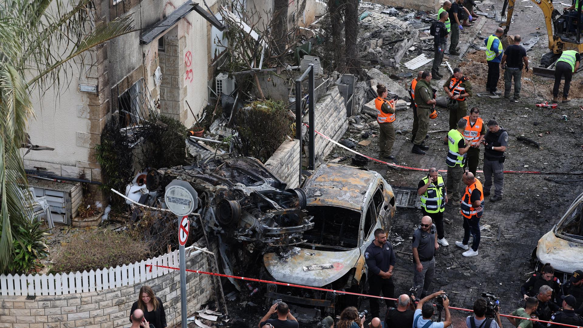 Männer stehen in gelben und orangen Schutzwesten nach einem Raketenangriff der Hisbollah in einem zerstörten Teil der israelischen Stadt Haifa. Männer stehen in gelben und orangen Schutzwesten nach einem Raketenangriff der Hisbollah in einem zerstörten Teil der israelischen Stadt Haifa.