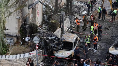 Männer stehen in gelben und orangen Schutzwesten nach einem Raketenangriff der Hisbollah in einem zerstörten Teil der israelischen Stadt Haifa.