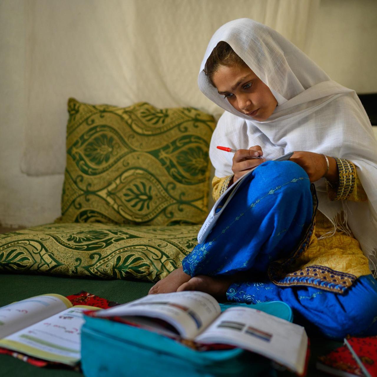 Die zehnjährige Hajira aus der afghanischen Provinz Nangarhar sitzt in einem Haus in einem abgelegenen Dorf östlich von Kabul über Schulbüchern und lernt.