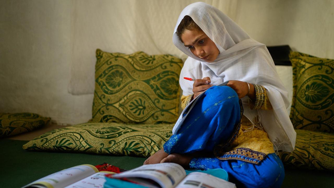 Die zehnjährige Hajira aus der afghanischen Provinz Nangarhar sitzt in einem Haus in einem abgelegenen Dorf östlich von Kabul über Schulbüchern und lernt.