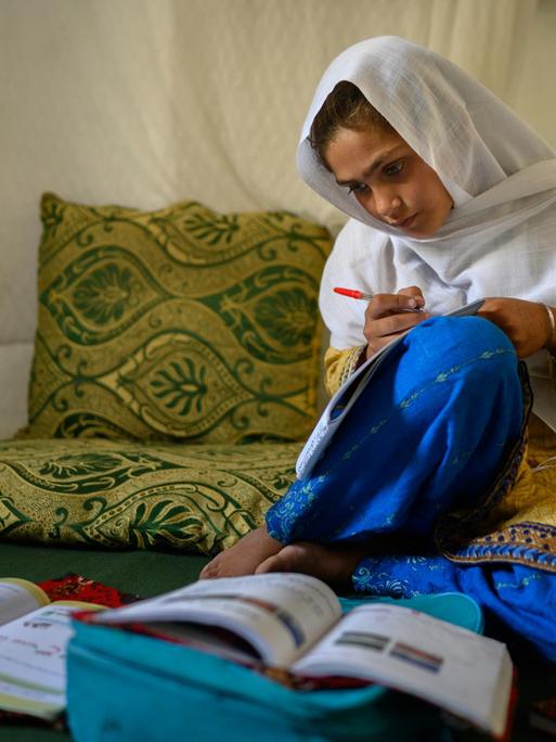 Die zehnjährige Hajira aus der afghanischen Provinz Nangarhar sitzt in einem Haus in einem abgelegenen Dorf östlich von Kabul über Schulbüchern und lernt.