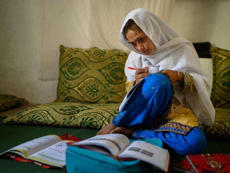 Die zehnjährige Hajira aus der afghanischen Provinz Nangarhar sitzt in einem Haus in einem abgelegenen Dorf östlich von Kabul über Schulbüchern und lernt.