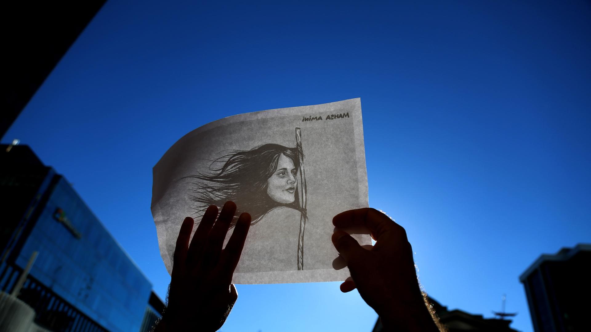 Eine Person hält eine weiße Fahne in die Luft auf der eine Zeichnung von Mahsa Amini zu sehen ist.