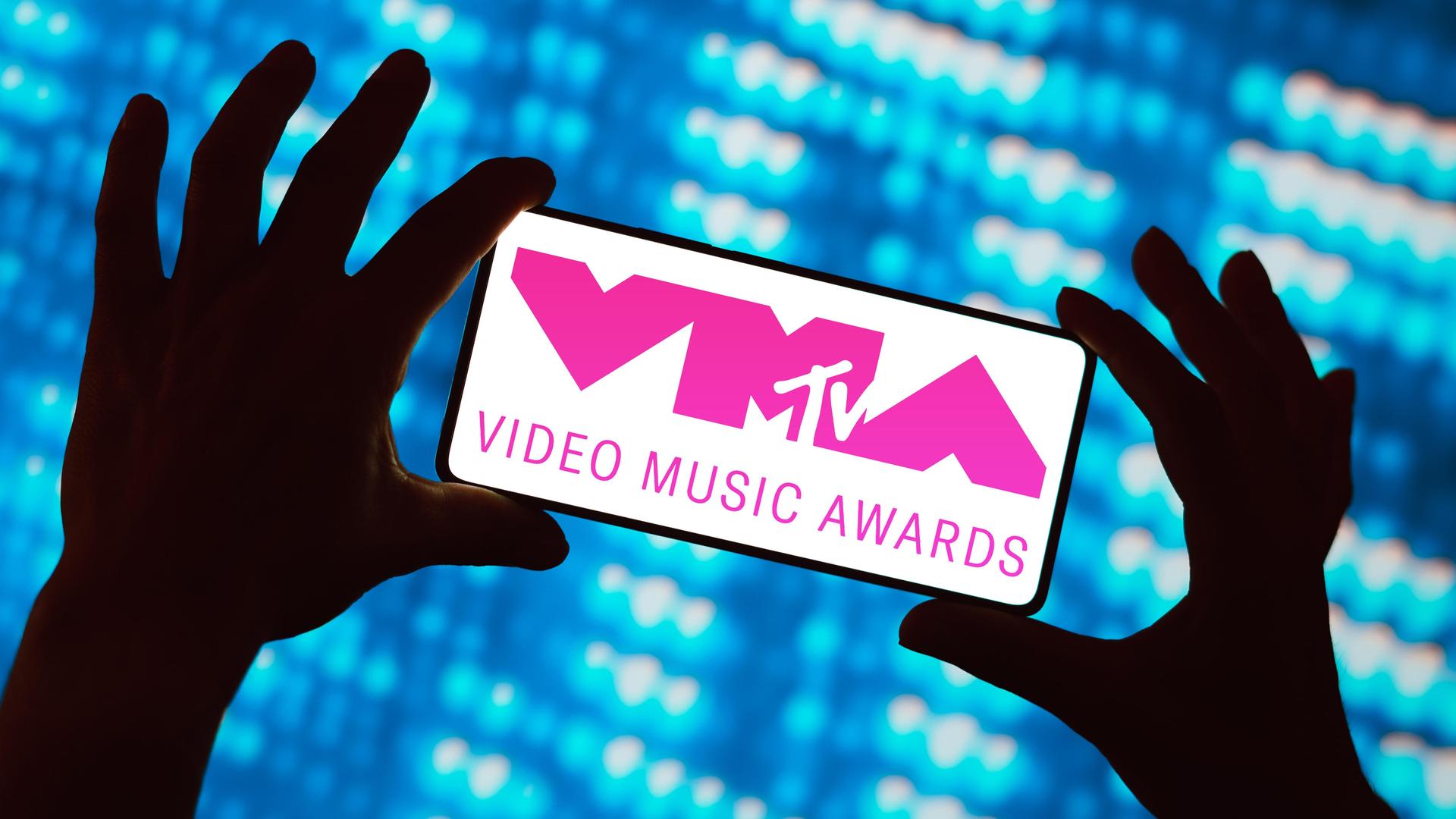 Das Logo der MTV Video Music Awards (VMA) ist auf dem Bildschirm eines Smartphones zu sehen, hochgehalten von zwei Händen mit gespreitzen Fingern vor einer mit blauen Pixeln erleuchteten Digitalwand Das Logo der MTV Video Music Awards (VMA) ist auf dem Bildschirm eines Smartphones zu sehen, hochgehalten von zwei Händen mit gespreitzen Fingern vor einer mit blauen Pixeln erleuchteten Digitalwand
