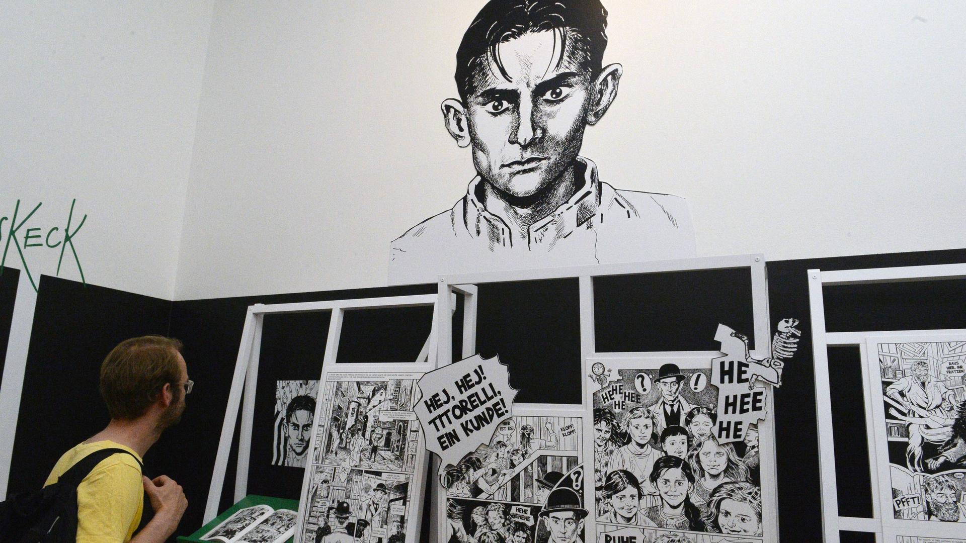 Ein junger Mann schaut sich Comic-Zeichnungen von Kafka in einer Ausstellung an.