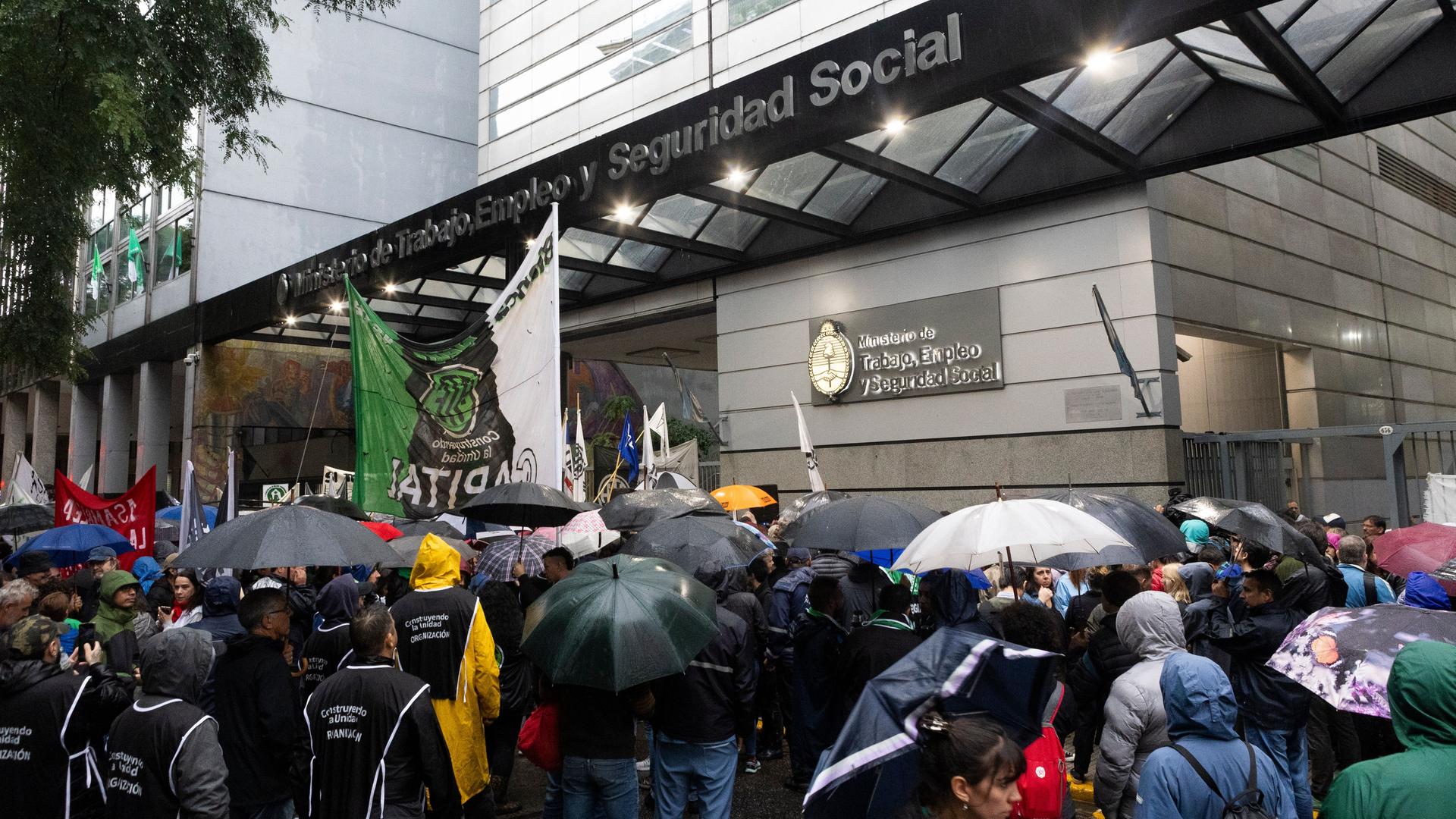 Demonstranten drängen sich vor dem Eingang des Ministeriums und halten unter Regenschirmen Transparente hoch
