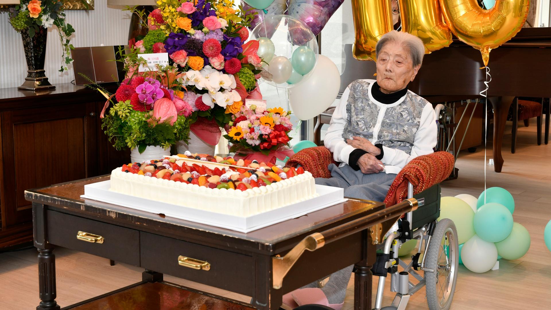 Das Bild zeigt die älteste Frau der Welt, Tomiko Itooka, die im Rollstuhl vor einer großen Geburtstagstorte sitzt. 