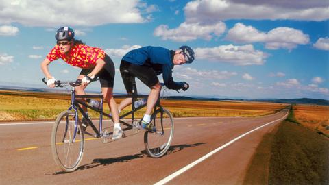 Einr Fahrradfahrerin und ein Fahrradfahrer steuern auf  ihrem Tandem in entgegengesetzte Richtungen.