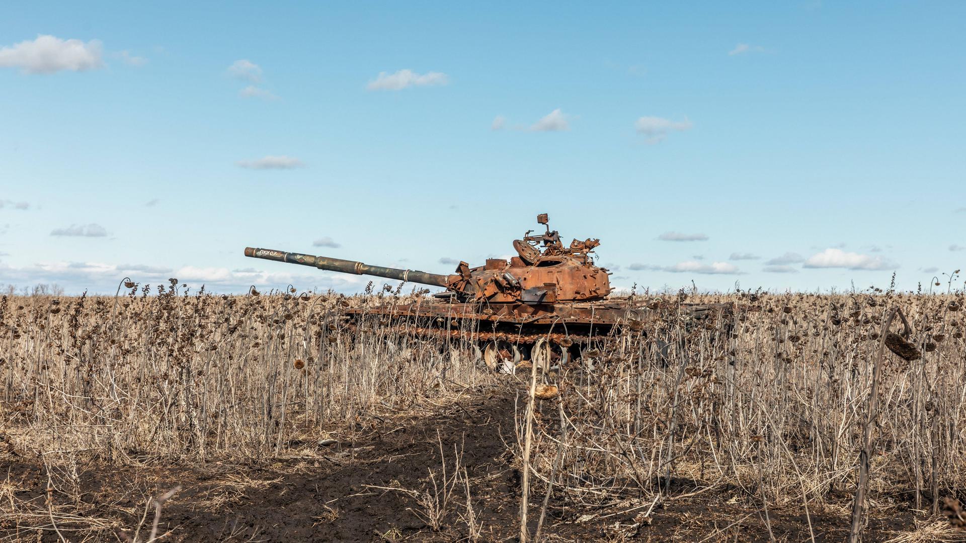 Der rostige Panzer steht auf einem Feld unter blauem Himmel.