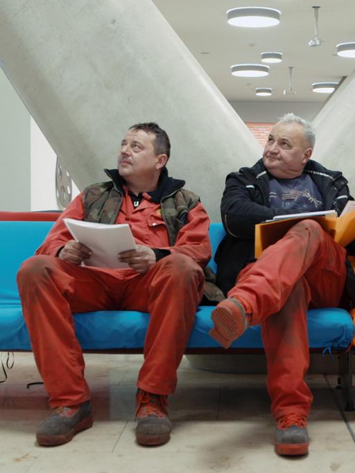 Drei Männer sitzen in einer Wartehalle.