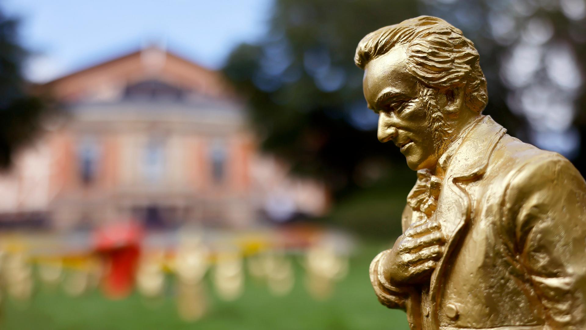 Eine goldene Richard-Wagner-Figuren stehen vor dem Festspielhaus. Der Komponist hat seine recht Hand auf die Brust gelegt und neigt sich leicht nach vorn. Eine goldene Richard-Wagner-Figuren stehen vor dem Festspielhaus. Der Komponist hat seine recht Hand auf die Brust gelegt und neigt sich leicht nach vorn.
