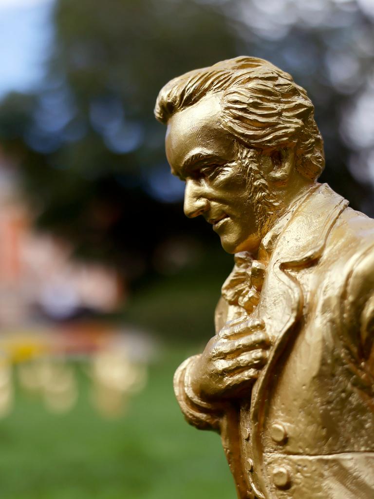 Eine goldene Richard-Wagner-Figuren stehen vor dem Festspielhaus. Der Komponist hat seine recht Hand auf die Brust gelegt und neigt sich leicht nach vorn.