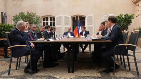Treffen zwischen Bundeskanzler Merz und Frankreichs Präsident Macron. Beide sitzen mit einer Delegation am Tisch.