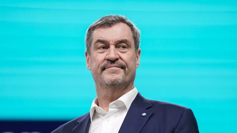 Markus Söder steht im dunklen Anzug auf einer Bühne vor einem leuchtend blauen Hintergrund.