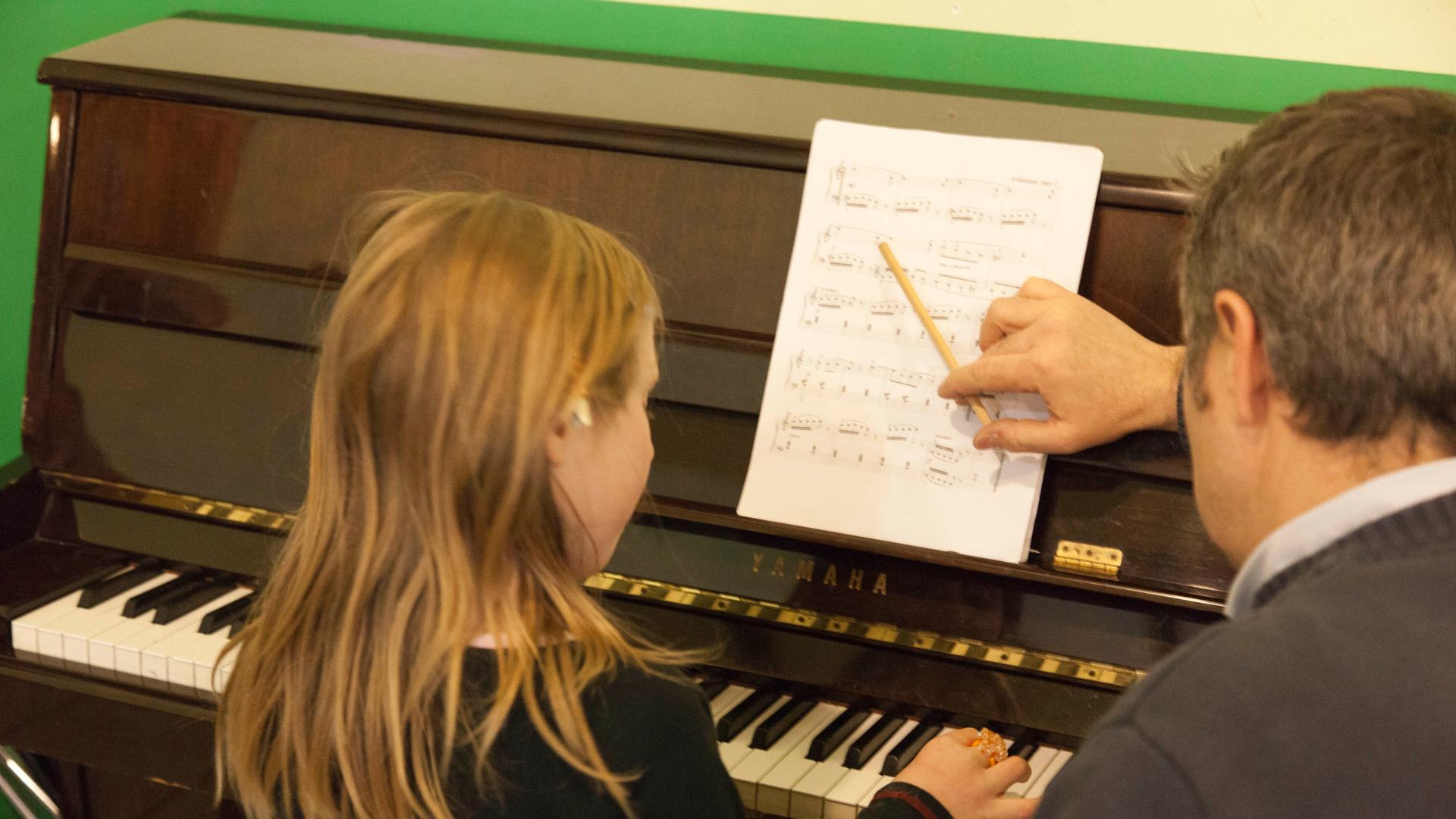Ein Mädchen beim Klavierunterricht, rechts neben ihr der Lehrer Ein Mädchen beim Klavierunterricht, rechts neben ihr der Lehrer
