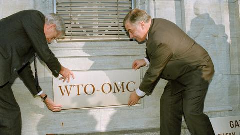 Ein Archivfoto vom 30. Dezember 1994: Zwei Männer befestigen in Genf eine Tafel an einer Hauswand mit dem Logo der neu gegründeten Welthandelsorganisation (WTO).
