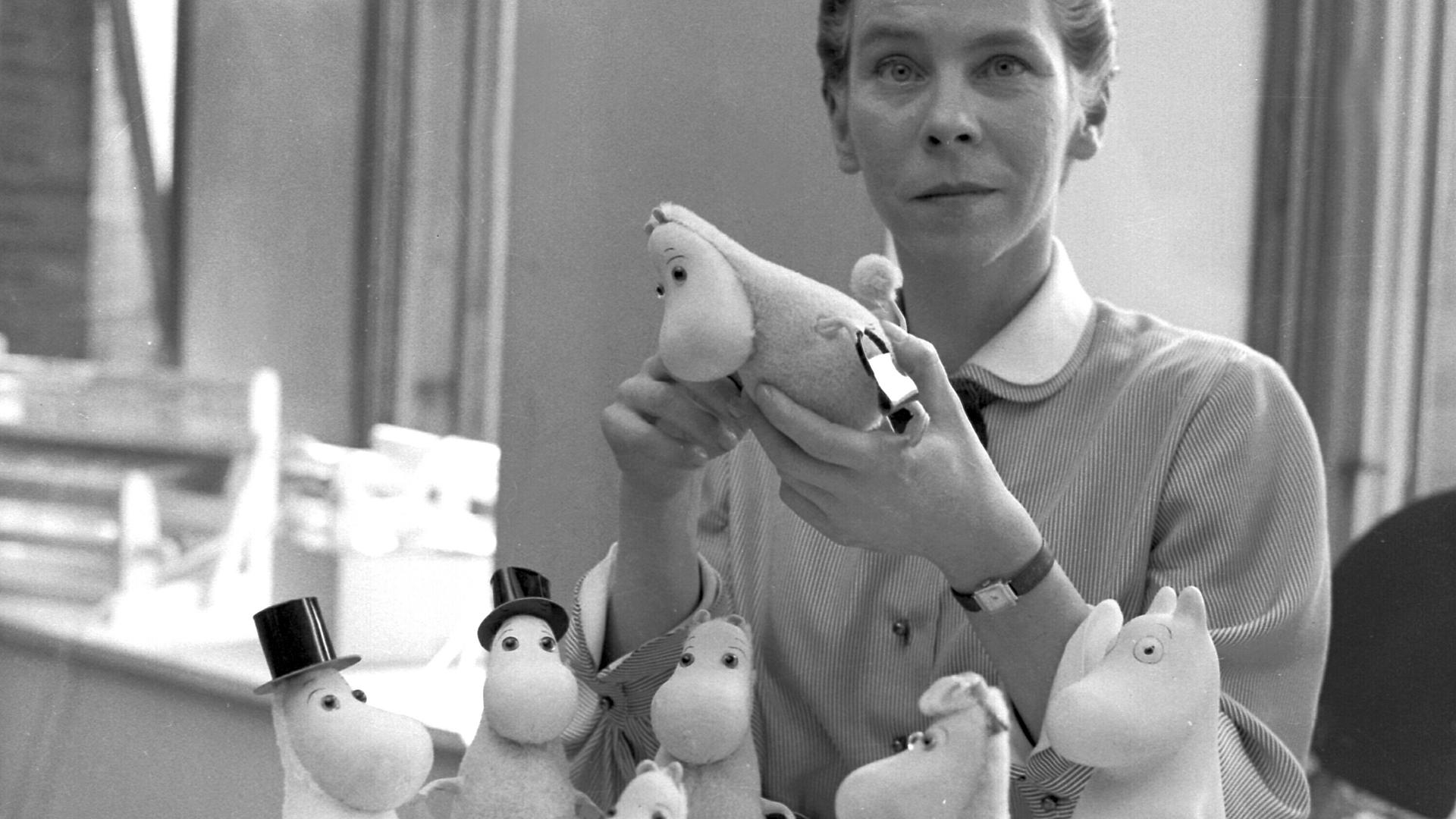 Die Künstlerin Tove Jansson zeigt auf einem Schwarz-weiß-Foto aus dem Jahr 1956 die von ihr erfundenen Mumins-Figuren.
