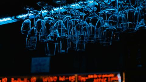 Blick auf eine Bar, wo kopfüber aufgehangene Gläser im bläulichen Licht schillern.