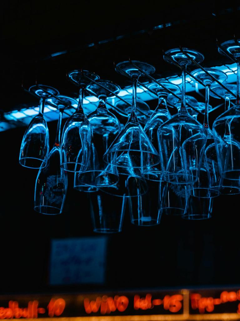 Blick auf eine Bar, wo kopfüber aufgehangene Gläser im bläulichen Licht schillern.