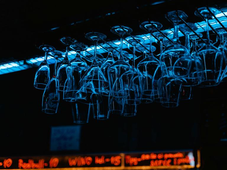 Blick auf eine Bar, wo kopfüber aufgehangene Gläser im bläulichen Licht schillern.