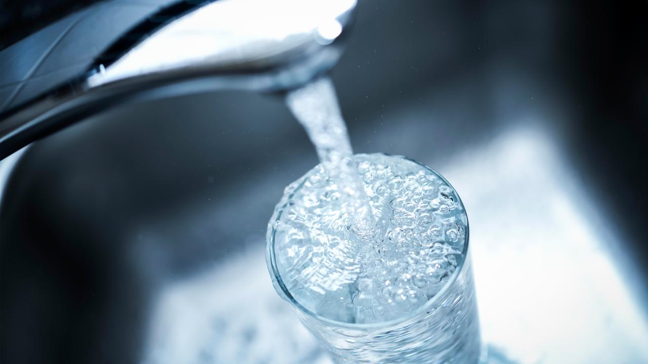Wasser läuft von einem Wasserhahn in ein Glas.