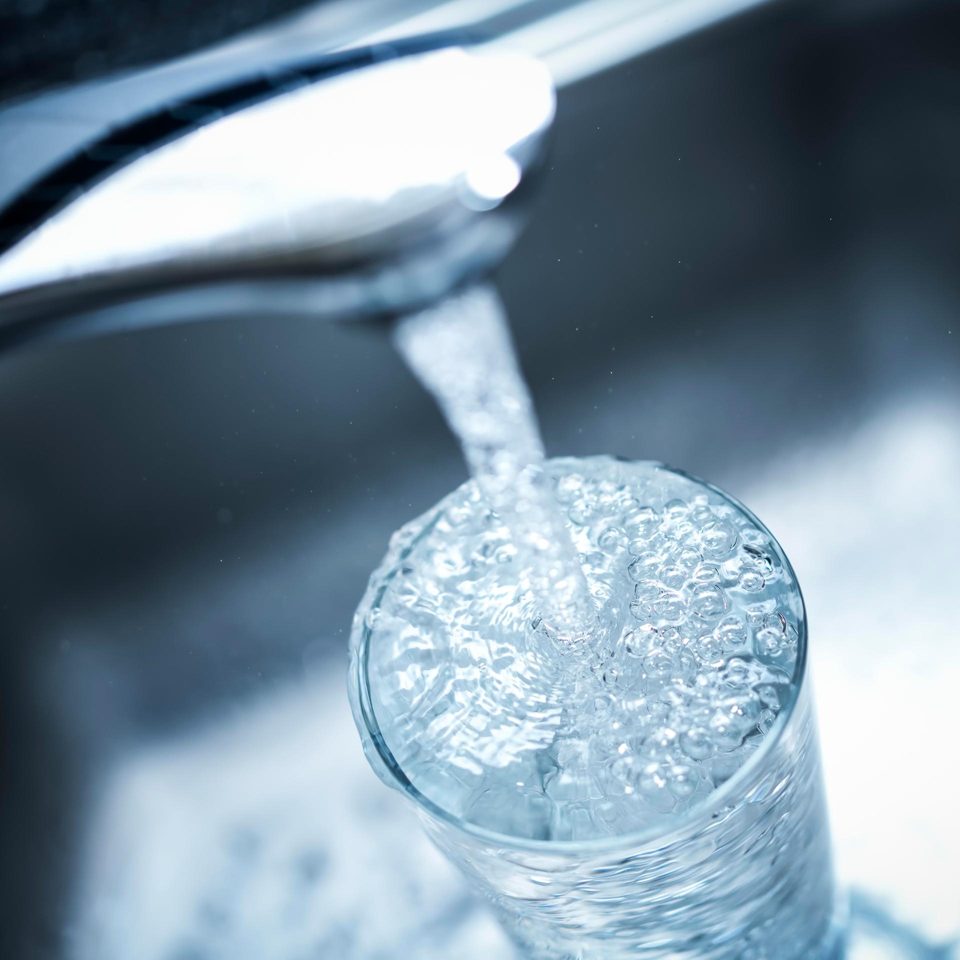 Wasser läuft von einem Wasserhahn in ein Glas.