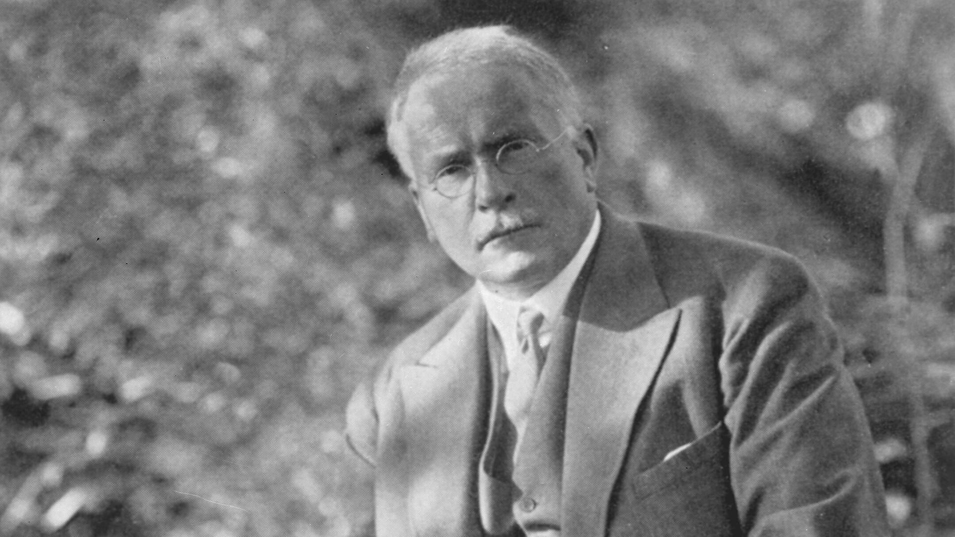 Carl Gustav Jung sitzt im Garten und hält seine Pfeife in der Hand.