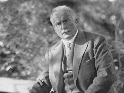 Carl Gustav Jung sitzt im Garten und hält seine Pfeife in der Hand.