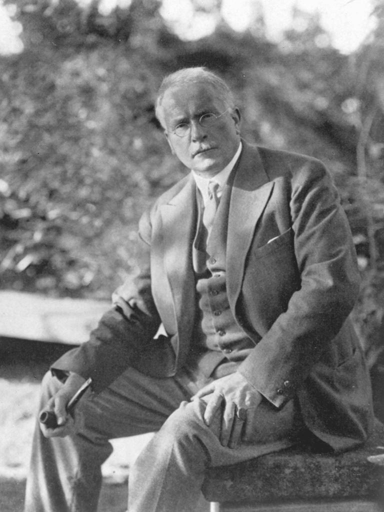 Carl Gustav Jung sitzt im Garten und hält seine Pfeife in der Hand.