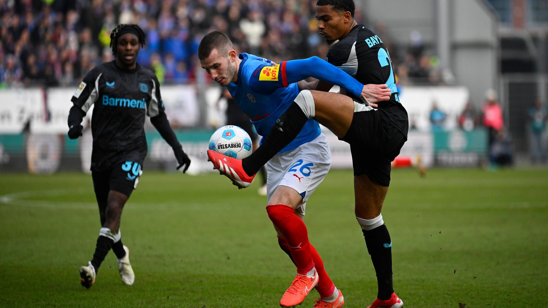 Zwei Spiel eng hintereinander, der Ball befindet sich vor dem vorderen Spieler auf Bauchhöhe, der hintere Spieler versucht den Ball mit dem linken Fuß zu erreichen.